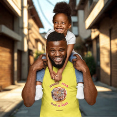 Dad in yellow “Donut Fear, Dad Is Here” QR code shirt with daughter on his shoulders, smiling in a city street.