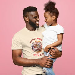 Father and daughter smiling at each other; dad wearing a cream-colored shirt with a donut QR code design that says “Donut Mess – Scan Me With Dad.”