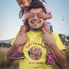Dad in a yellow t-shirt with a donut QR code and the text “Scan to Enter Dad Zone,” smiling as his daughter playfully covers his eyes.