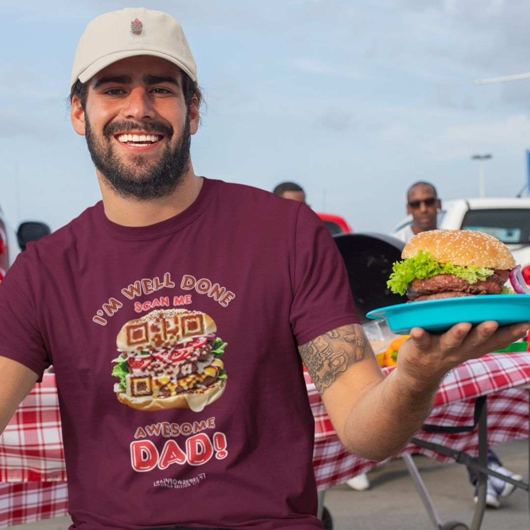 Dad wearing a maroon t-shirt with a QR code burger design and the phrase “I'm Well Done – Scan Me, Awesome Dad,” holding a burger and smiling at a BBQ.